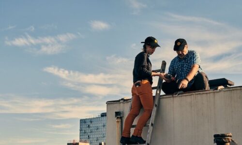 A woman and a man standing on a rooftop, gazing intently at an unseen object